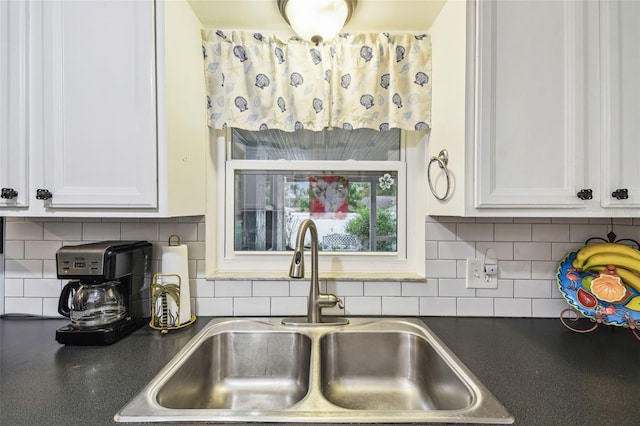 kitchen featuring dark countertops, decorative backsplash, white cabinets, and a sink