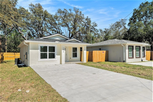 view of front of house with stucco siding, driveway, a front lawn, fence, and central AC unit