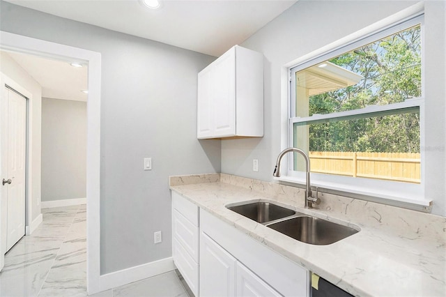 kitchen with light stone counters, marble finish floor, baseboards, and a sink