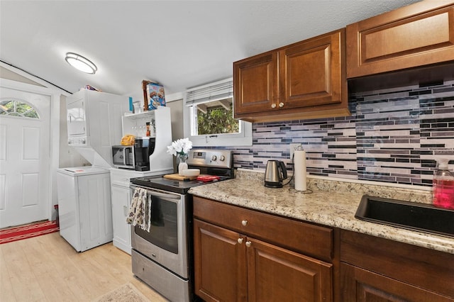 kitchen featuring stacked washer and dryer, electric stove, light wood-style flooring, and backsplash