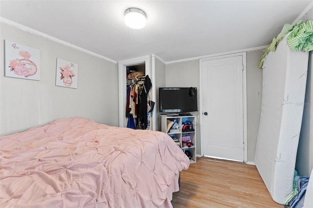 bedroom with a walk in closet, crown molding, wood finished floors, and a closet