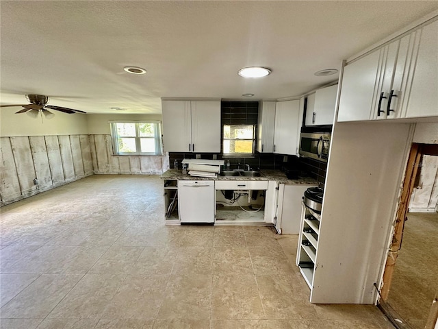 kitchen with dark countertops, a wainscoted wall, white dishwasher, white cabinets, and stainless steel microwave