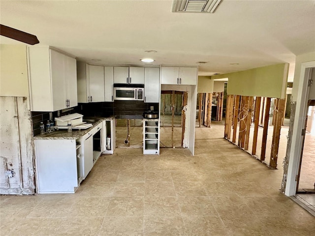 kitchen featuring stainless steel microwave, white cabinets, visible vents, and backsplash