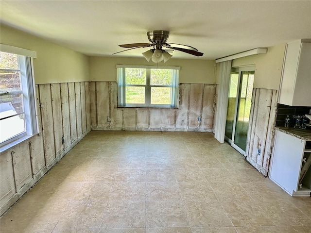 spare room with plenty of natural light, a ceiling fan, and a wainscoted wall