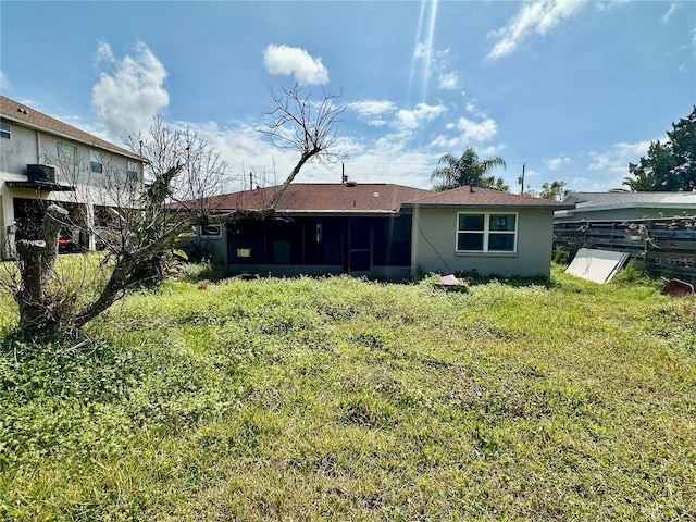 rear view of property featuring stucco siding, fence, a yard, and a sunroom