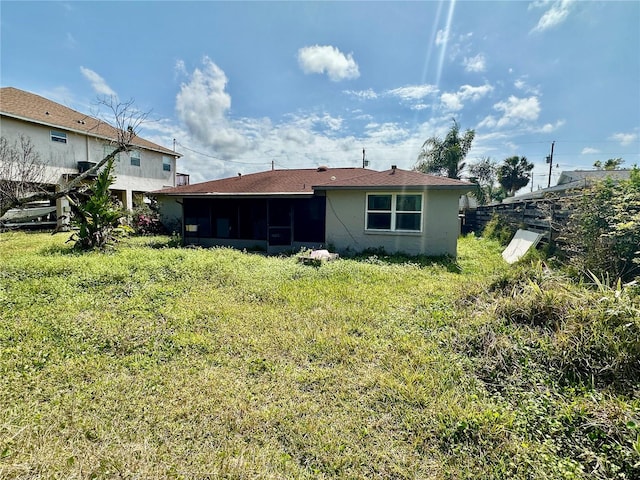 rear view of property with stucco siding, a lawn, and a sunroom