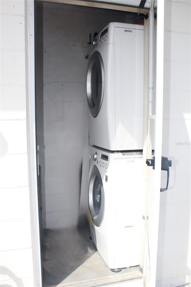 washroom featuring laundry area, stacked washer and clothes dryer, concrete block wall, and a garage