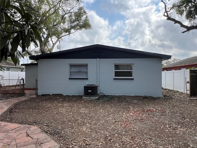 view of side of property with cooling unit, concrete block siding, and fence