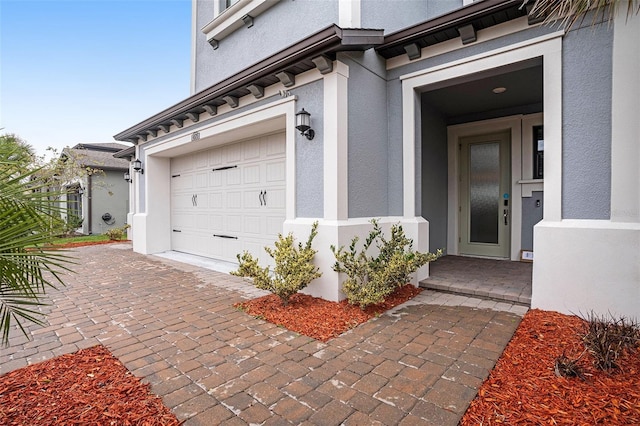 doorway to property with stucco siding, decorative driveway, and a garage