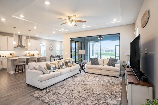 living area featuring a raised ceiling, recessed lighting, wood finished floors, and ceiling fan