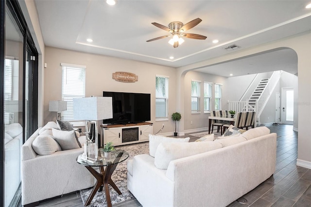 living area featuring a tray ceiling, arched walkways, visible vents, and a healthy amount of sunlight