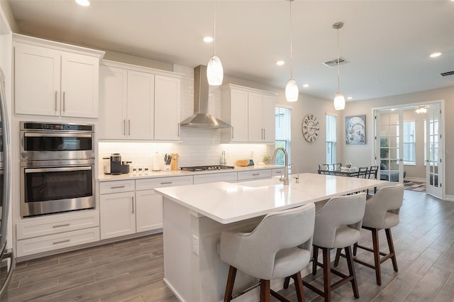 kitchen with visible vents, a sink, appliances with stainless steel finishes, wall chimney range hood, and tasteful backsplash