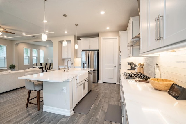 kitchen with dark wood finished floors, a sink, appliances with stainless steel finishes, under cabinet range hood, and open floor plan