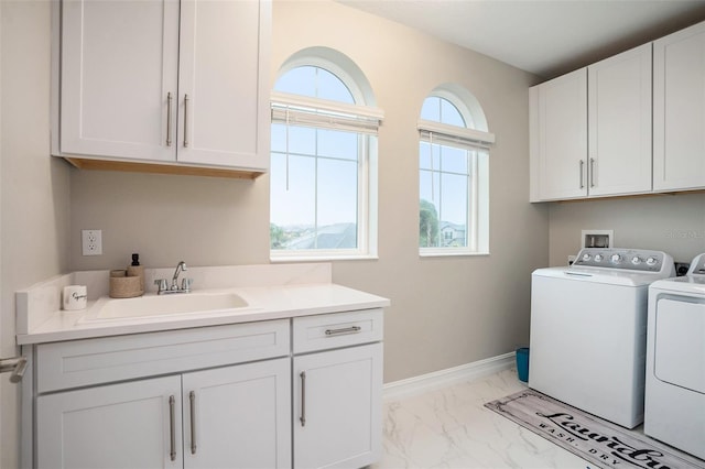 laundry area featuring baseboards, washing machine and clothes dryer, cabinet space, a sink, and marble finish floor