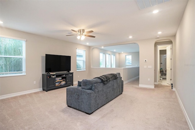 living area featuring a healthy amount of sunlight, baseboards, arched walkways, and light carpet