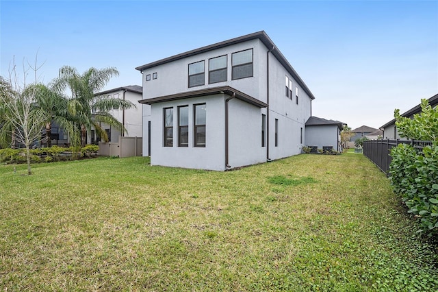 rear view of property with stucco siding, a yard, and fence