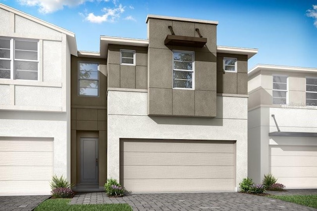 view of property featuring decorative driveway, an attached garage, and stucco siding