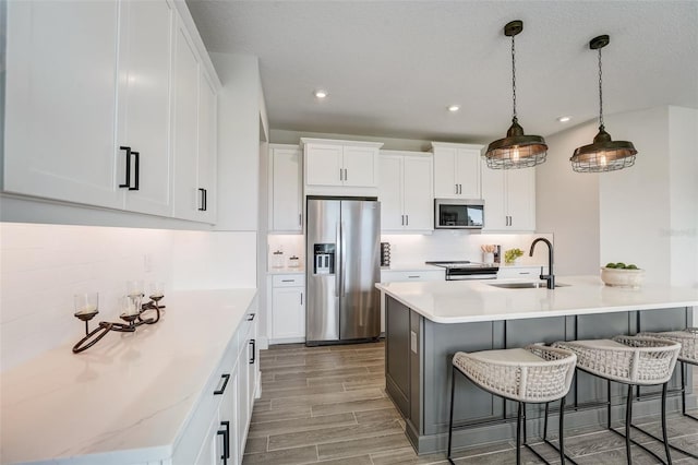 kitchen featuring tasteful backsplash, wood tiled floor, appliances with stainless steel finishes, white cabinets, and a sink