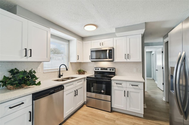 kitchen with white cabinetry, stainless steel appliances, light wood-style floors, and a sink