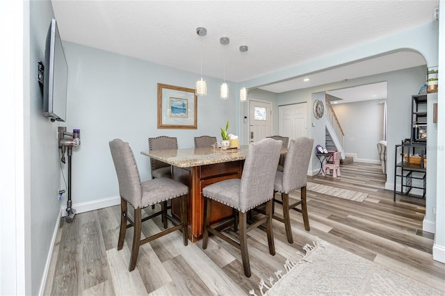 dining room with stairway, baseboards, a textured ceiling, and light wood finished floors