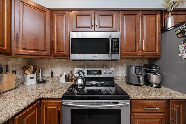 kitchen with light stone counters, brown cabinets, tasteful backsplash, and appliances with stainless steel finishes