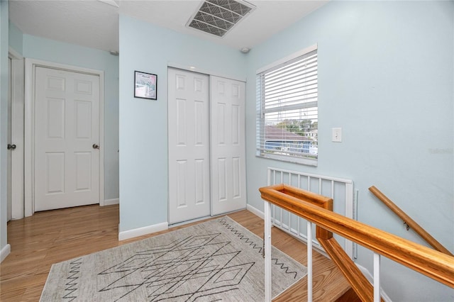 interior space featuring an upstairs landing, visible vents, baseboards, and wood finished floors