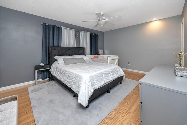 bedroom featuring light wood finished floors, a textured ceiling, a ceiling fan, and baseboards