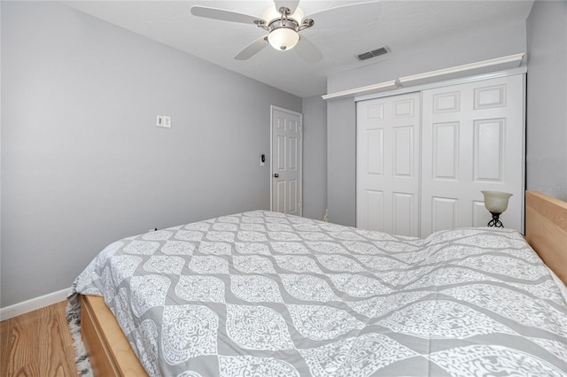 bedroom with visible vents, baseboards, wood finished floors, a closet, and a ceiling fan