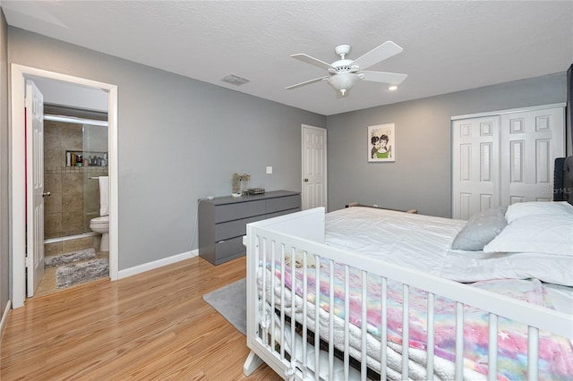 bedroom with visible vents, light wood finished floors, baseboards, ensuite bath, and a closet