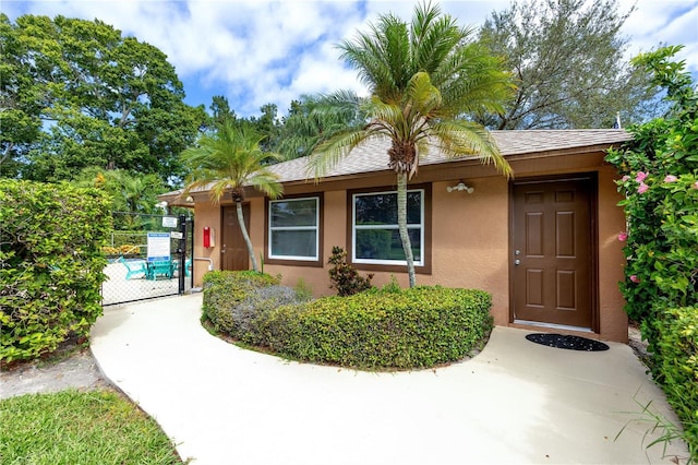 entrance to property featuring stucco siding, roof with shingles, and fence