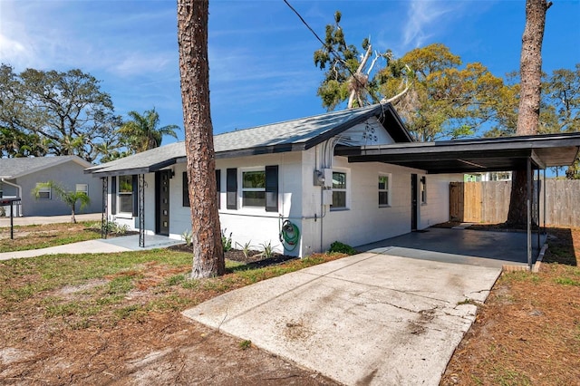 view of front of home with an attached carport, a shingled roof, fence, concrete block siding, and driveway