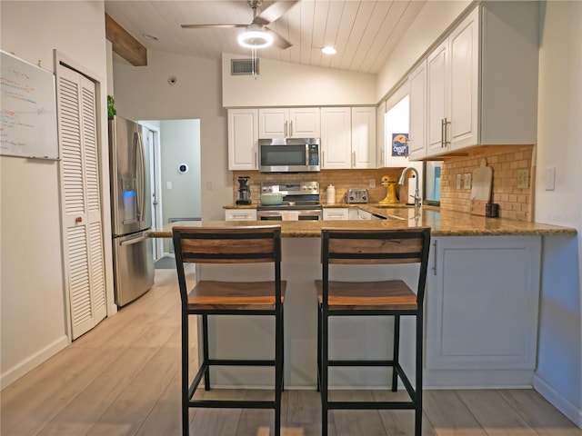 kitchen with a peninsula, a sink, vaulted ceiling, appliances with stainless steel finishes, and white cabinetry