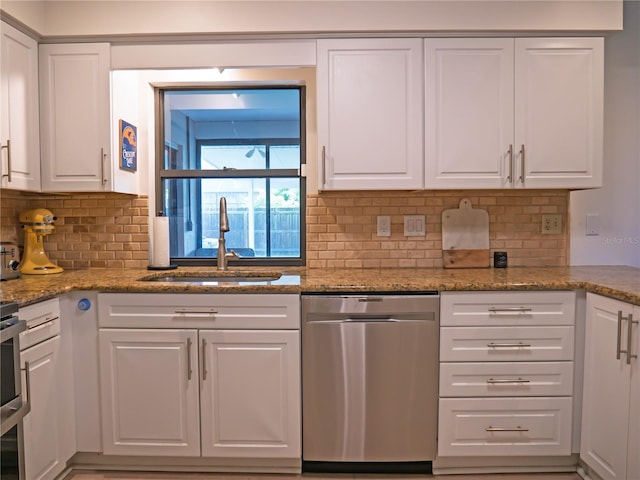 kitchen with backsplash, light stone countertops, dishwasher, white cabinets, and a sink