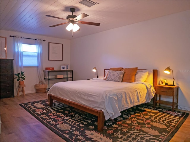 bedroom with ceiling fan, visible vents, baseboards, and wood finished floors