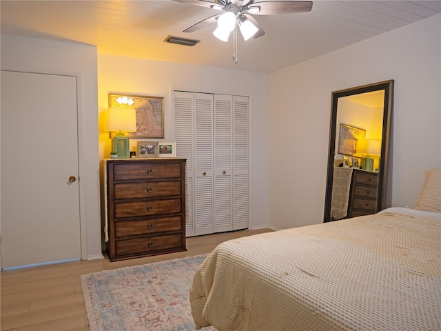 bedroom with a ceiling fan, wood finished floors, visible vents, and a closet