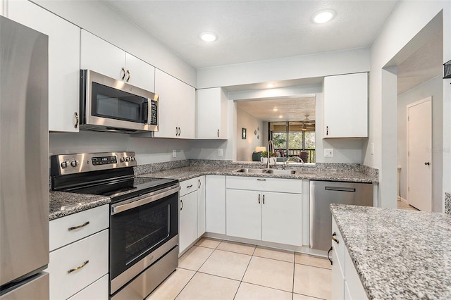 kitchen featuring light stone countertops, light tile patterned flooring, white cabinets, stainless steel appliances, and a sink