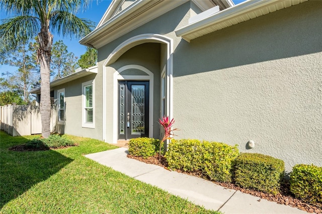 entrance to property featuring a yard, fence, and stucco siding