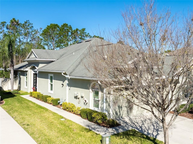 view of front facade featuring a shingled roof, a front lawn, concrete driveway, stucco siding, and a garage