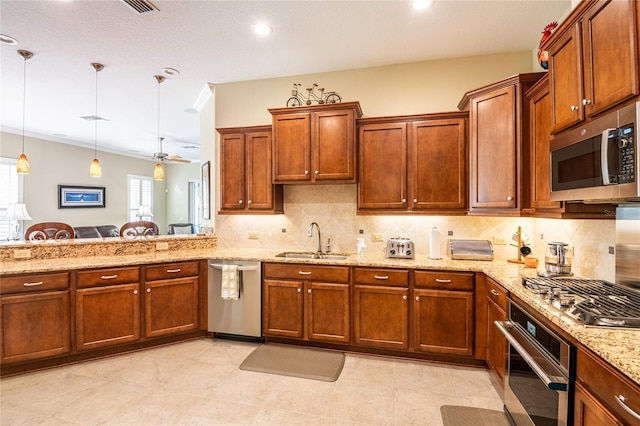 kitchen with light stone countertops, a sink, appliances with stainless steel finishes, pendant lighting, and tasteful backsplash