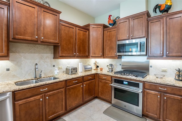 kitchen with a sink, stainless steel appliances, light stone counters, and decorative backsplash