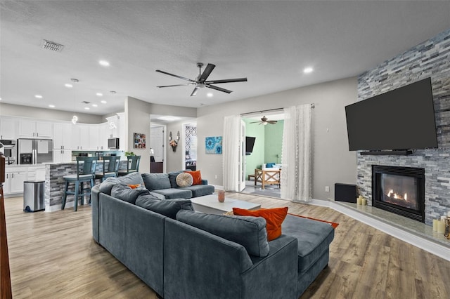 living room featuring visible vents, recessed lighting, a fireplace, a textured ceiling, and light wood-type flooring