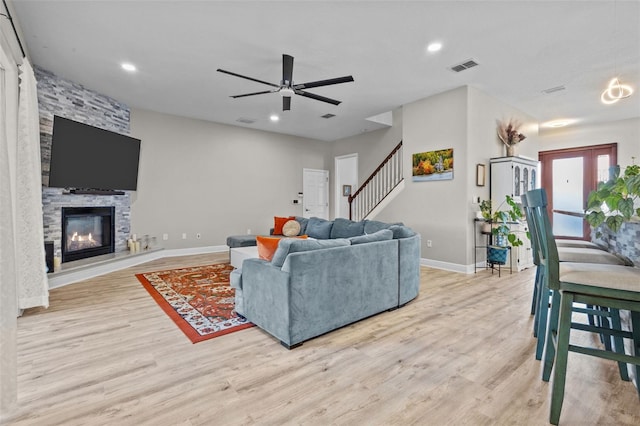 living room featuring visible vents, baseboards, stairway, a stone fireplace, and wood finished floors