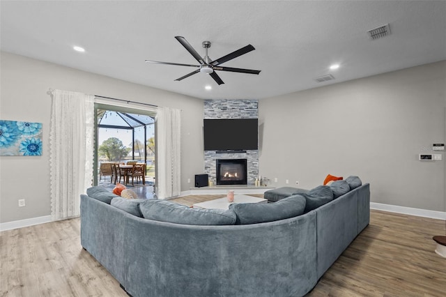 living room with visible vents, baseboards, ceiling fan, a stone fireplace, and light wood-style flooring