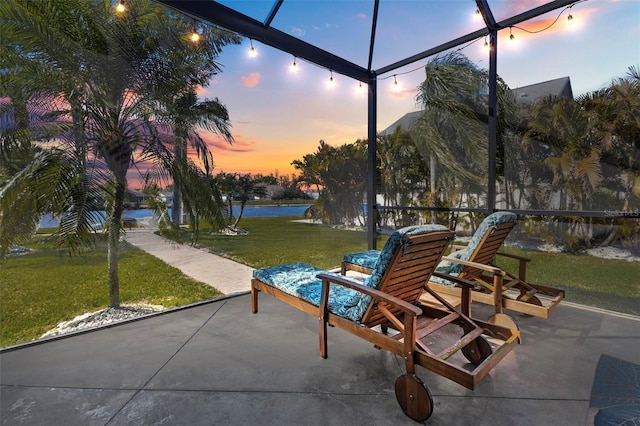 patio terrace at dusk with a yard, a water view, and a lanai