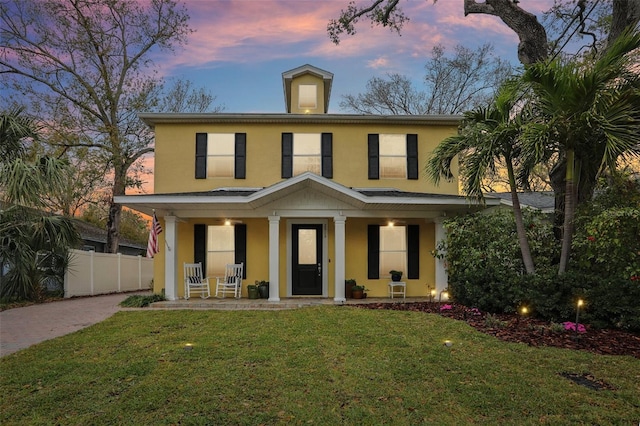 view of front of house with a front yard, fence, a porch, stucco siding, and decorative driveway