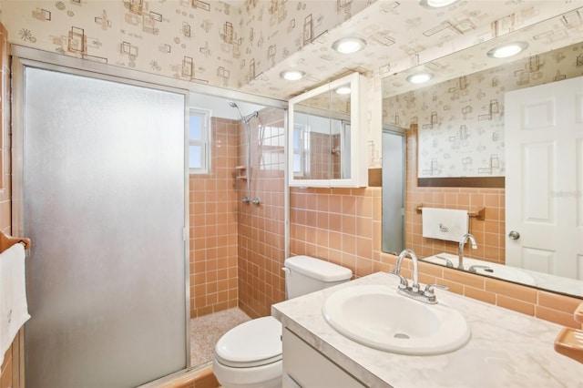 bathroom featuring toilet, a stall shower, tile walls, wainscoting, and wallpapered walls