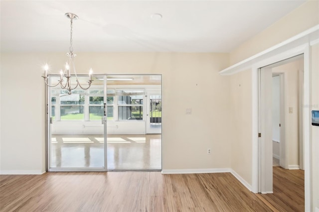 unfurnished dining area featuring baseboards, a notable chandelier, and wood finished floors