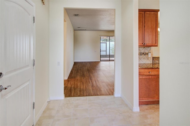 corridor featuring light tile patterned floors, visible vents, and baseboards