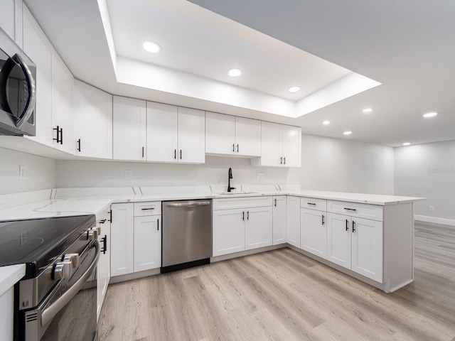 kitchen featuring a sink, light wood-type flooring, appliances with stainless steel finishes, and a peninsula