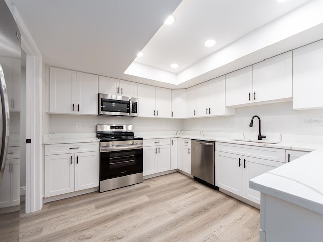 kitchen featuring light wood-style flooring, a sink, a tray ceiling, stainless steel appliances, and white cabinets